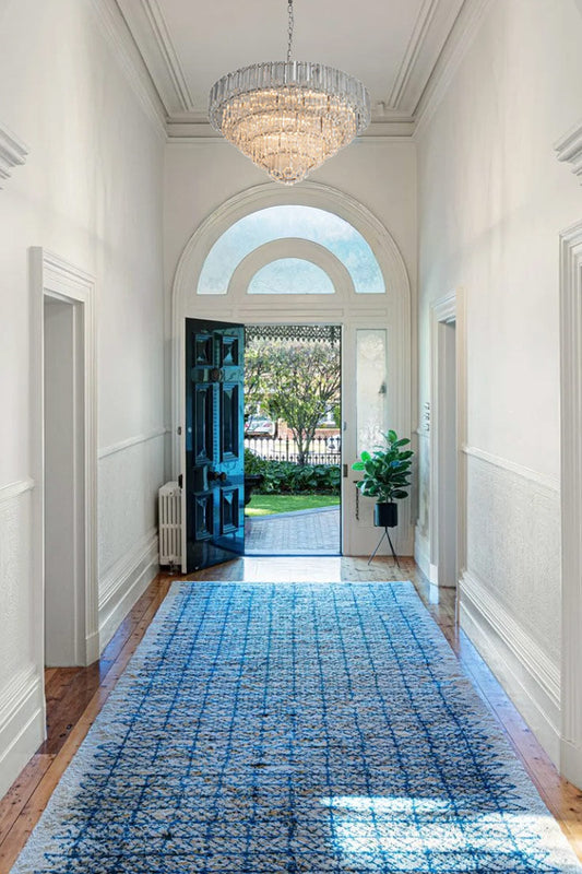 Extra large glass chandelier in an entry hallway with traditional white walls ans arched mouling with a blue carpet runner. 