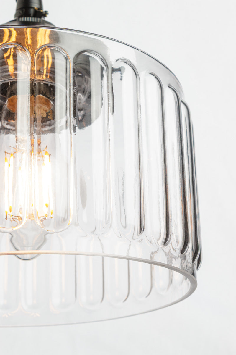 Close-up of a clear fluted glass pendant light shade with visible warm Edison-style bulbs inside