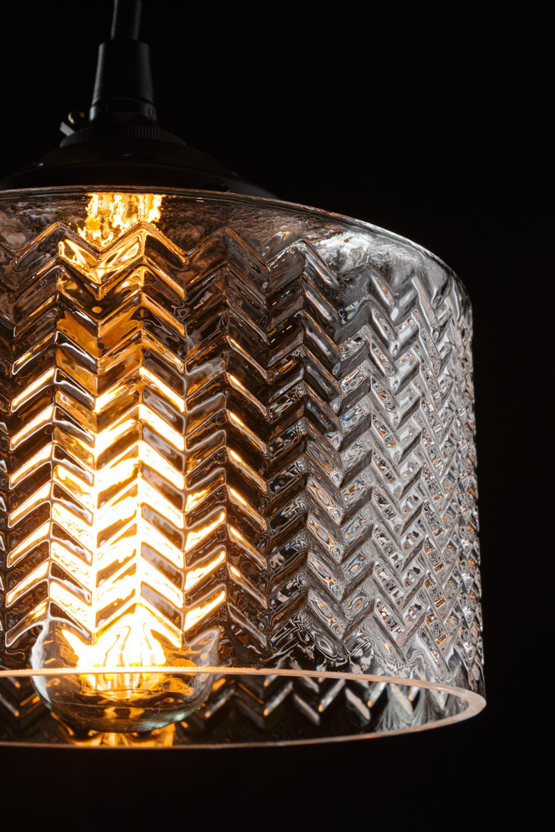 Close up of clear shade, showcasing the chevron detailing in a dark room with a clear bulb. 