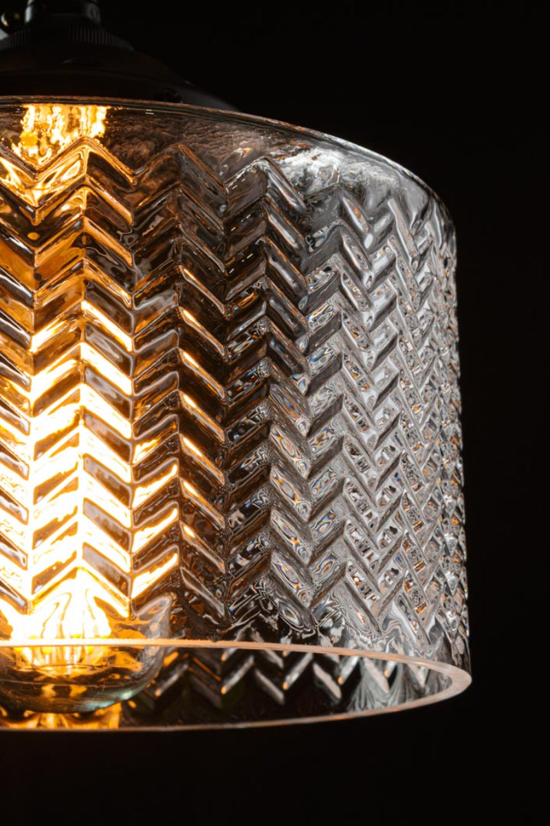 Close up of the clear glass shade, illuminated in a dark studio space. 