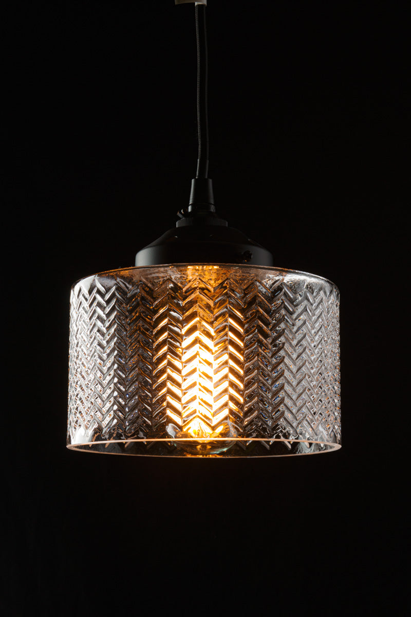 Clear glass shade on a black pendant cord in a dark room showcasing the intricate chevron detailing.