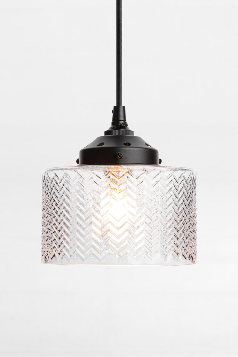 Clear glass shade with chevron detailing on a black pendant cord and gallery. 