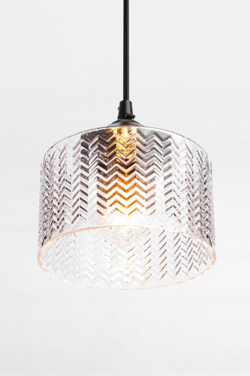 Open ended cylindrical, clear glass shade with chevron detailing on a black pendant cord.