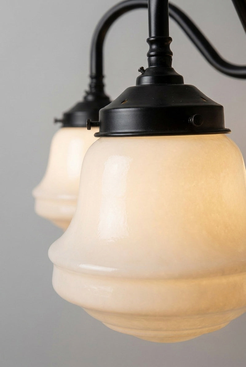 Close-up of an illuminated Colton Schoolhouse opal glass shade fitted to the black gooseneck chandelier.