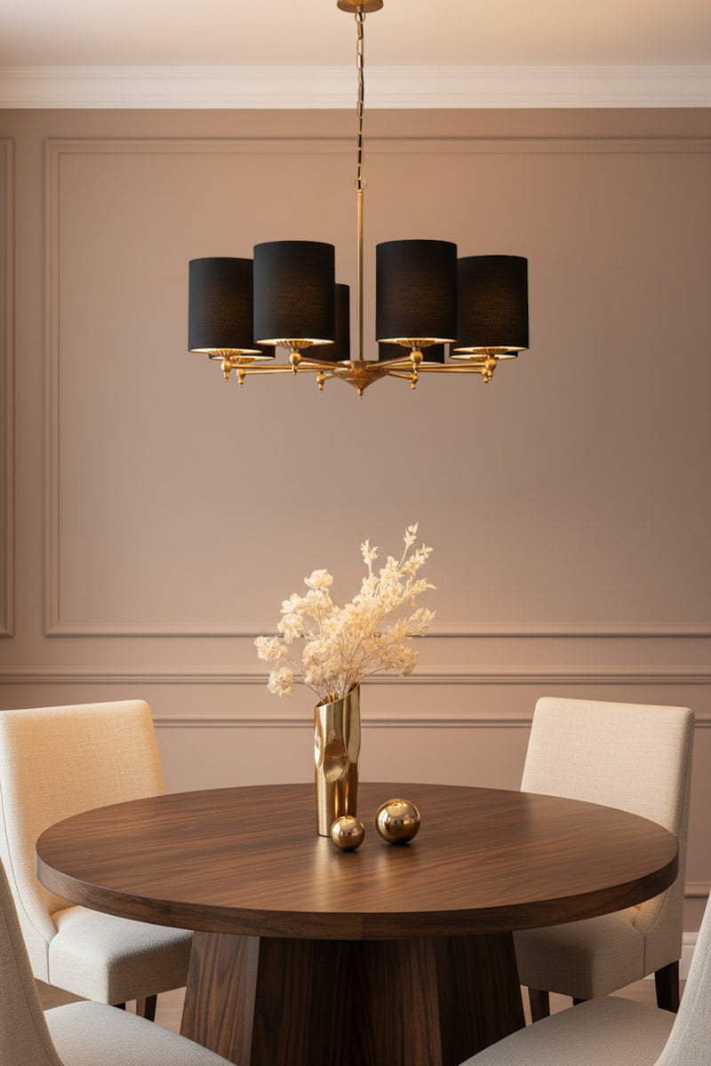 8 light antique gold chandelier with black cotton shades over a circular walnut dining table and cream chairs. 
