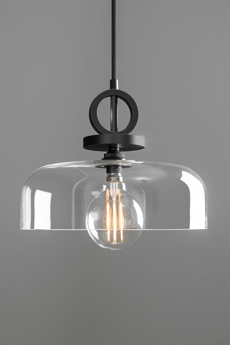 Front view of the Dixon NYC Glass Pendant Light in matt black, showcasing its shallow clear glass dome and distinctive circular metal detailing.