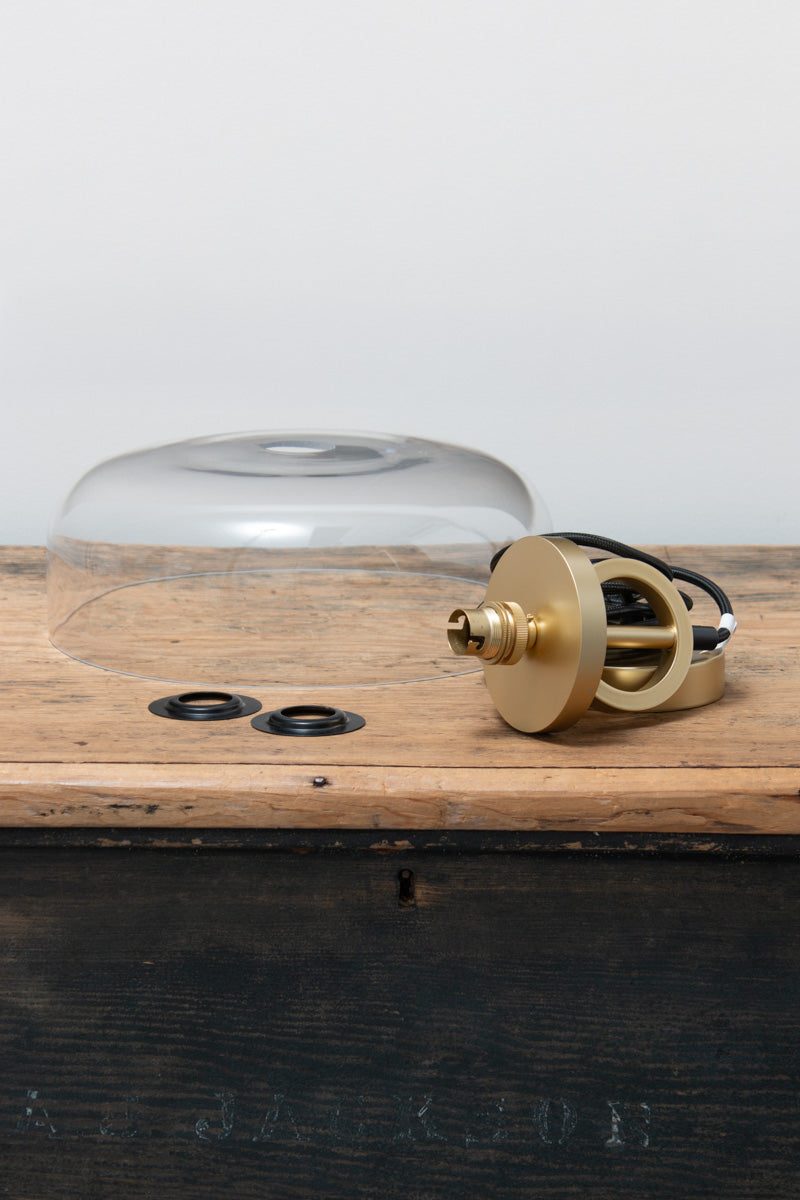 Dixon NYC Glass Pendant Light components featuring a clear glass dome shade and gold/brass ring and disc suspension with black braided cord.