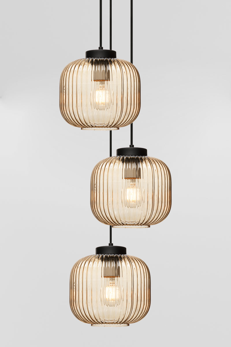 Three drop pendant light with reeded glass shades in amber and black hardware. 