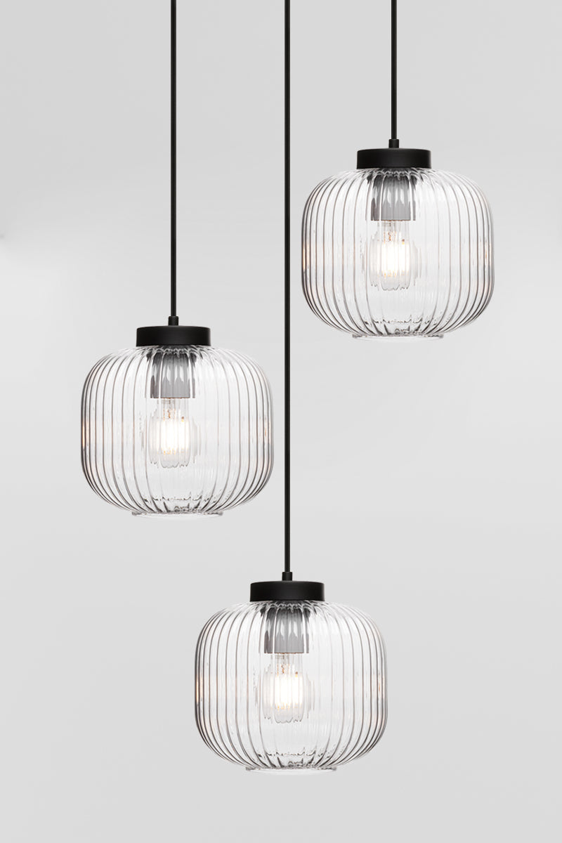 Three drop pendant light with reeded glass shades in clear and black hardware. 