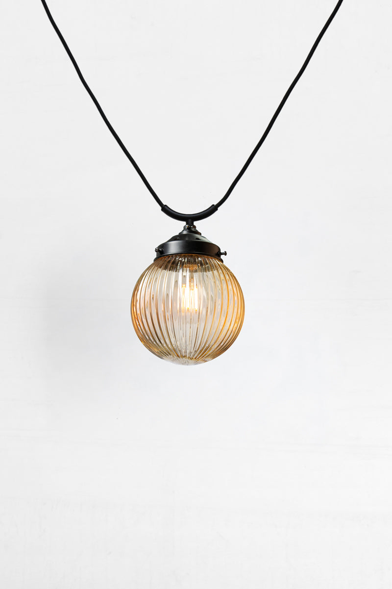 Amber glass ball shade with reeded detailing on a black trapeze style pendant cord. 