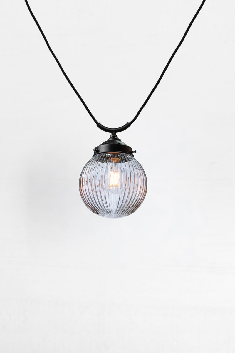 Clear glass ball shade with reeded detailing on a black trapeze style pendant cord. 