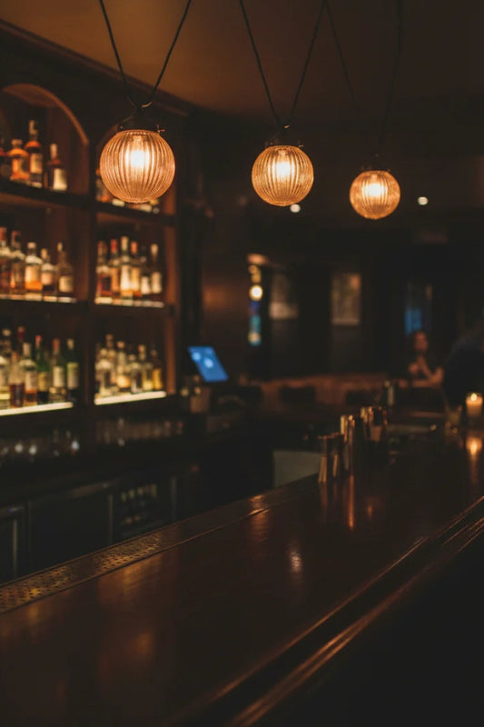 Three amber glass all shades on black trapeze pendant cords over a moody bar area. 
