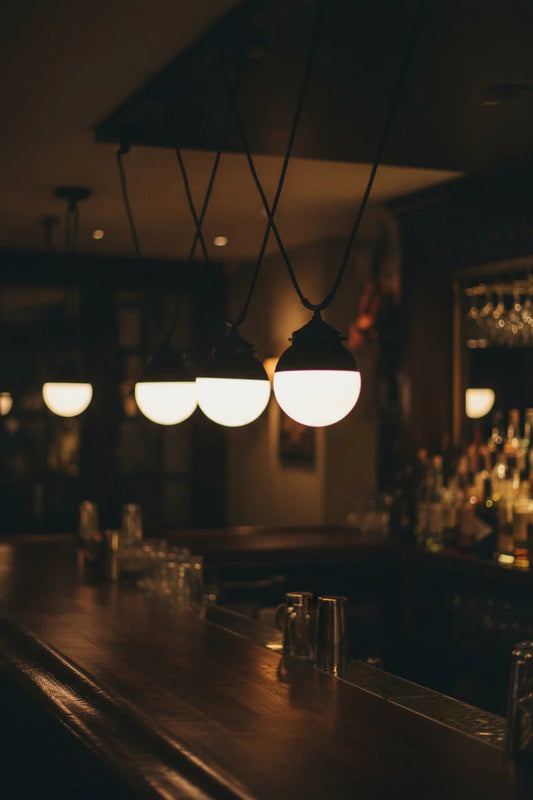 Multiple trapeze pendant cords with black crown shpere glass shades over a bar area