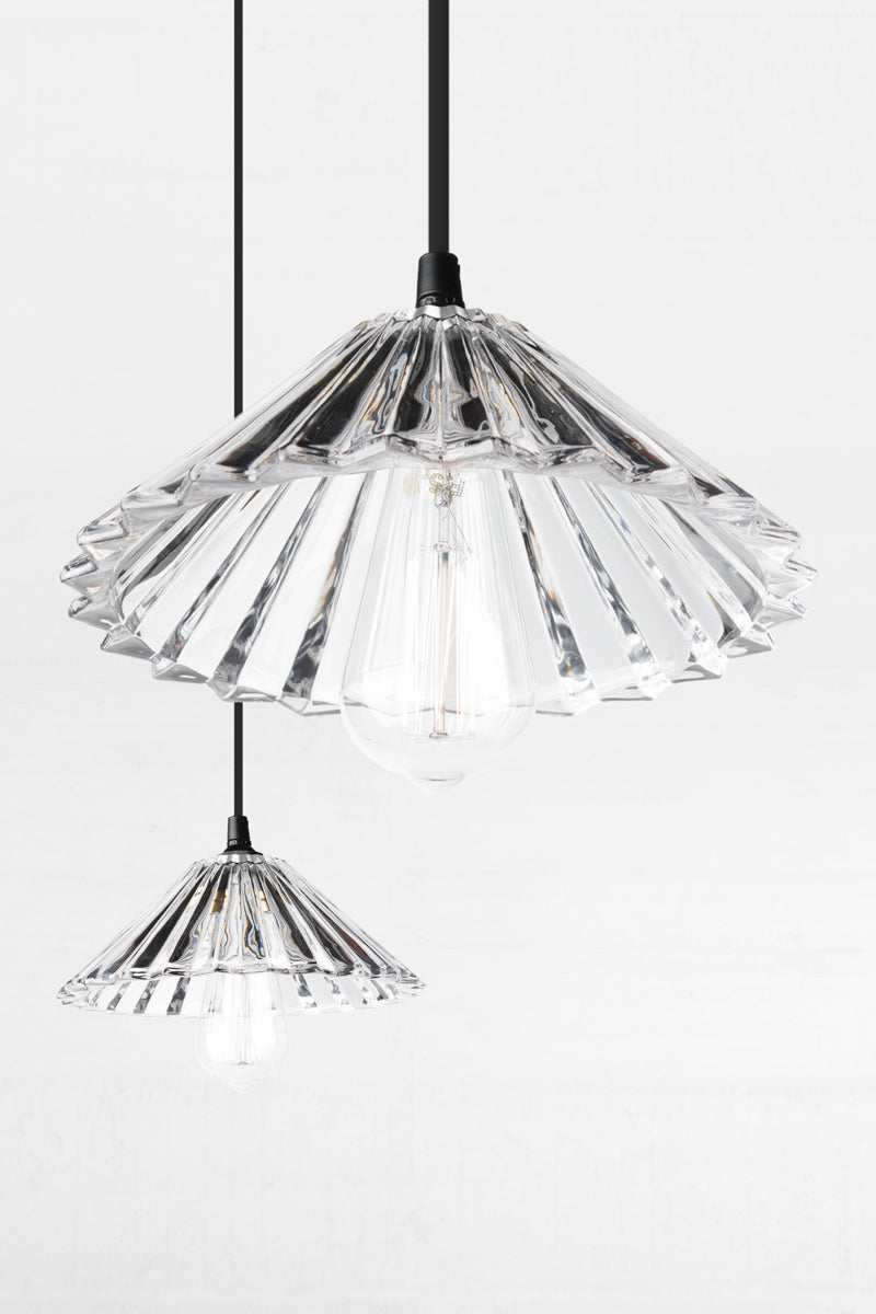 Close up of two clear glass pleated shades with teardrop bulbs. 