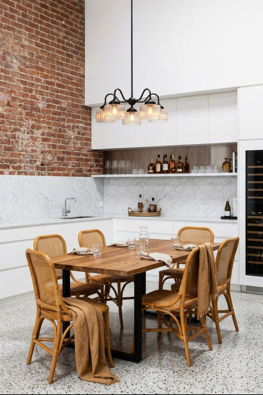 Black five-arm Capri Glass Gooseneck Chandelier with clear fluted glass shades, suspended above a timber dining table in a modern kitchen with exposed brick, marble splashback and terrazzo flooring.