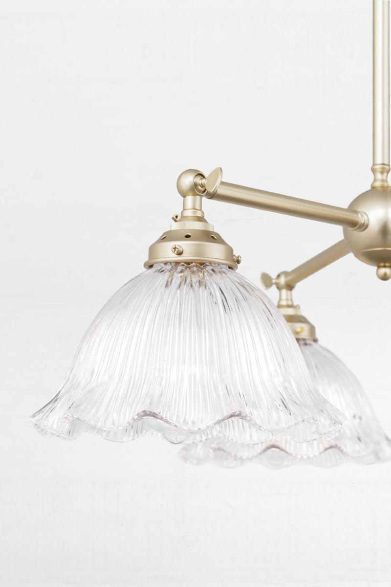 Close up of the gold/brass 3 arm chandelier with adjustable lampholders, paired with reeded clear glass shades with a frilled edge