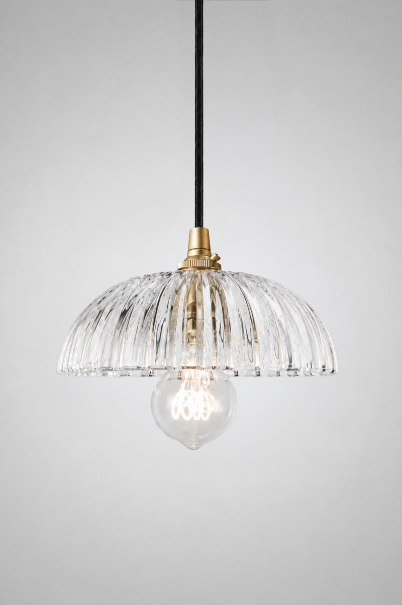 Deloraine clear glass pendant light on a black gold pendant cord, illuminated to showcase soft light refraction through the ridged pressed glass shade.