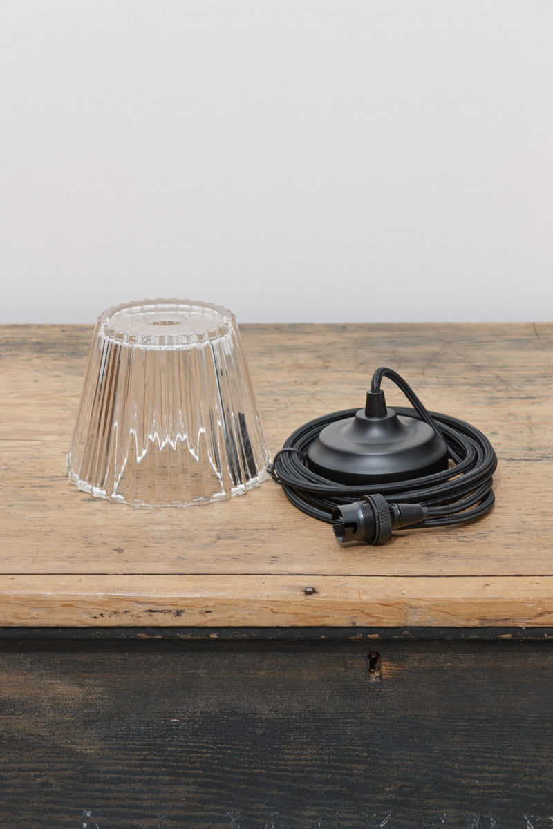 Overhead view of clear ribbed glass shade and black pendant fitting components on rustic timber surface.