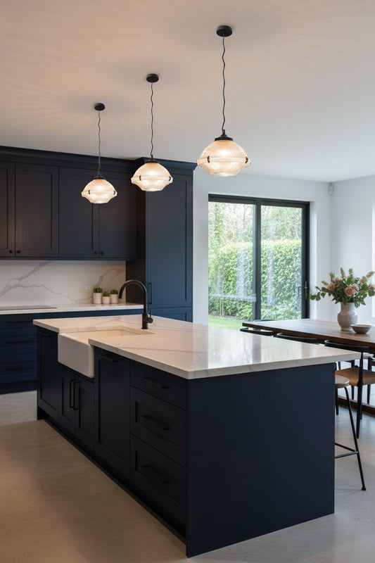 Thre industrial style pendant lights with holophane and ribbed glass, paired with black metalware over a navy and white marble kitchen. 