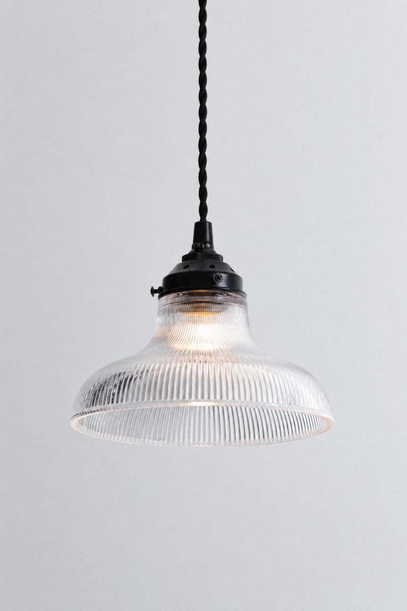 Small clear glass shade with ridged detailing on a black gallery with twisted black cloth cord. 