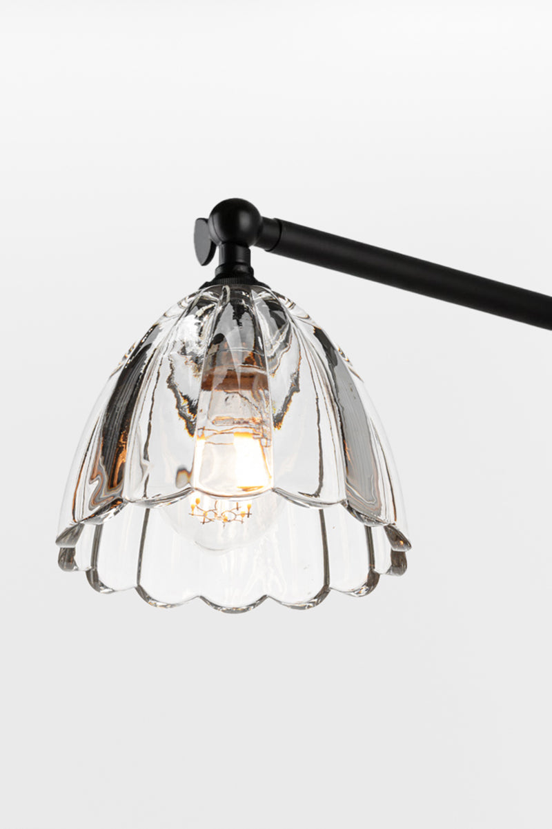 Close up of the black chandelier arm with the clear glass shade with scalloped edge. 
