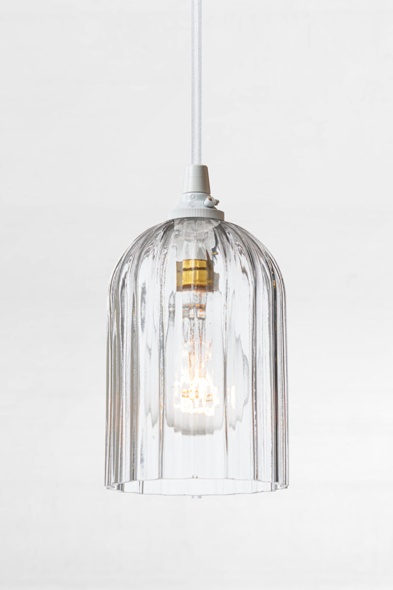 Clear glass elongated shade with fluted detailing, paired with a white pendant cord and clear bulb. 
