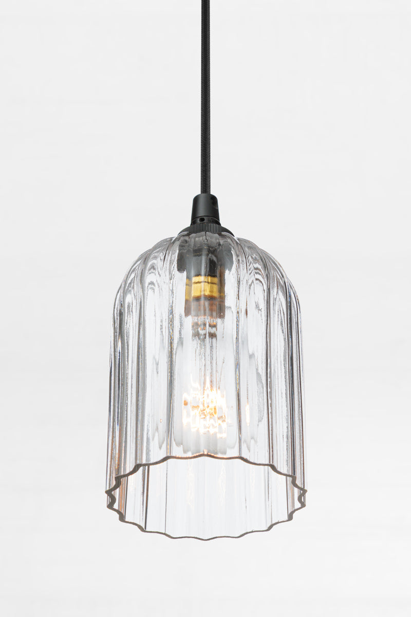 Clear glass elongated shade with fluted detailing, paired with a black pendant cord and clear bulb. 
