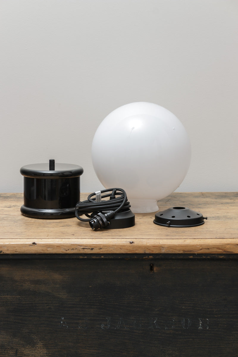 Disassembled mediumopal glass ball shade, short black topper and pendant cord on a timber bench.