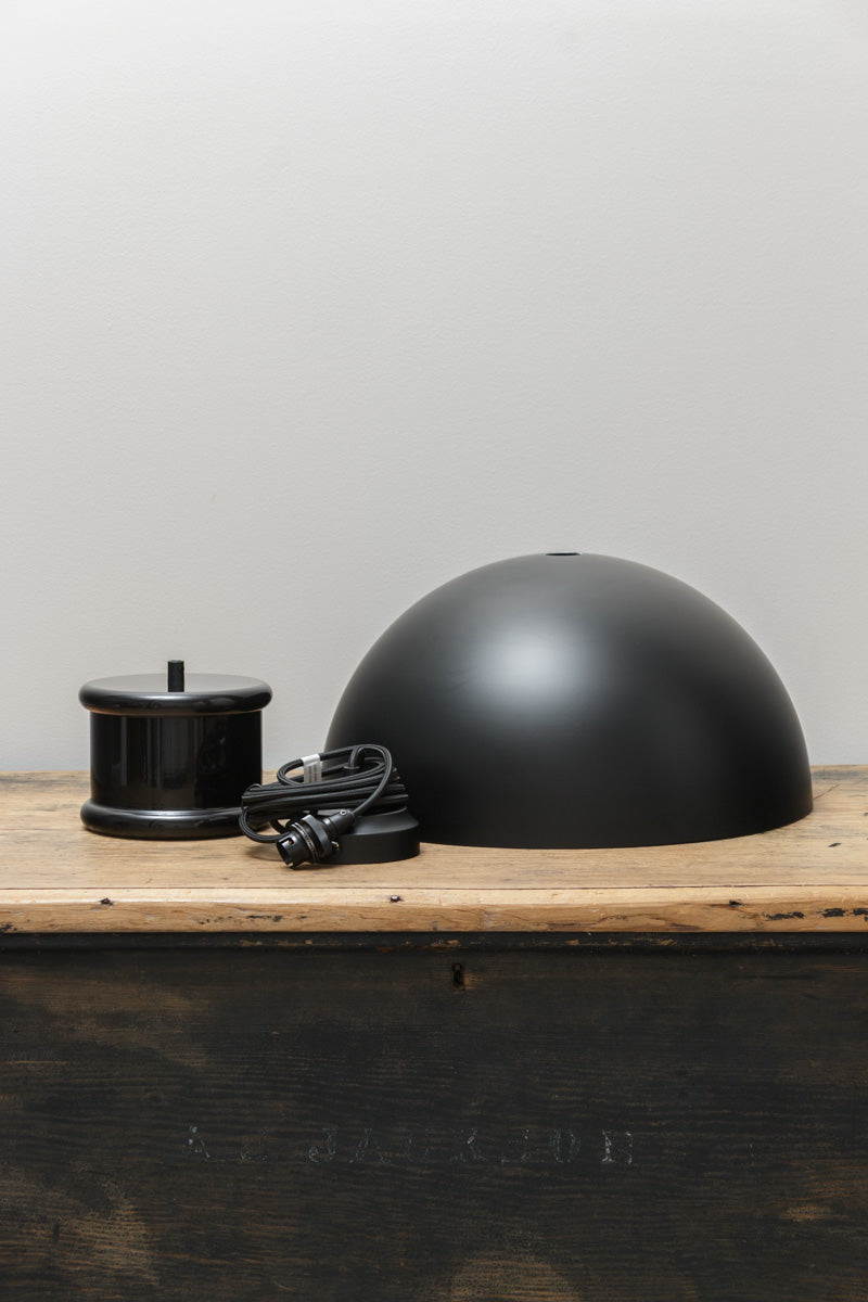 Detail view of the matt black industrial dome pendant light resting on a rustic timber surface showcasing its metal construction.
