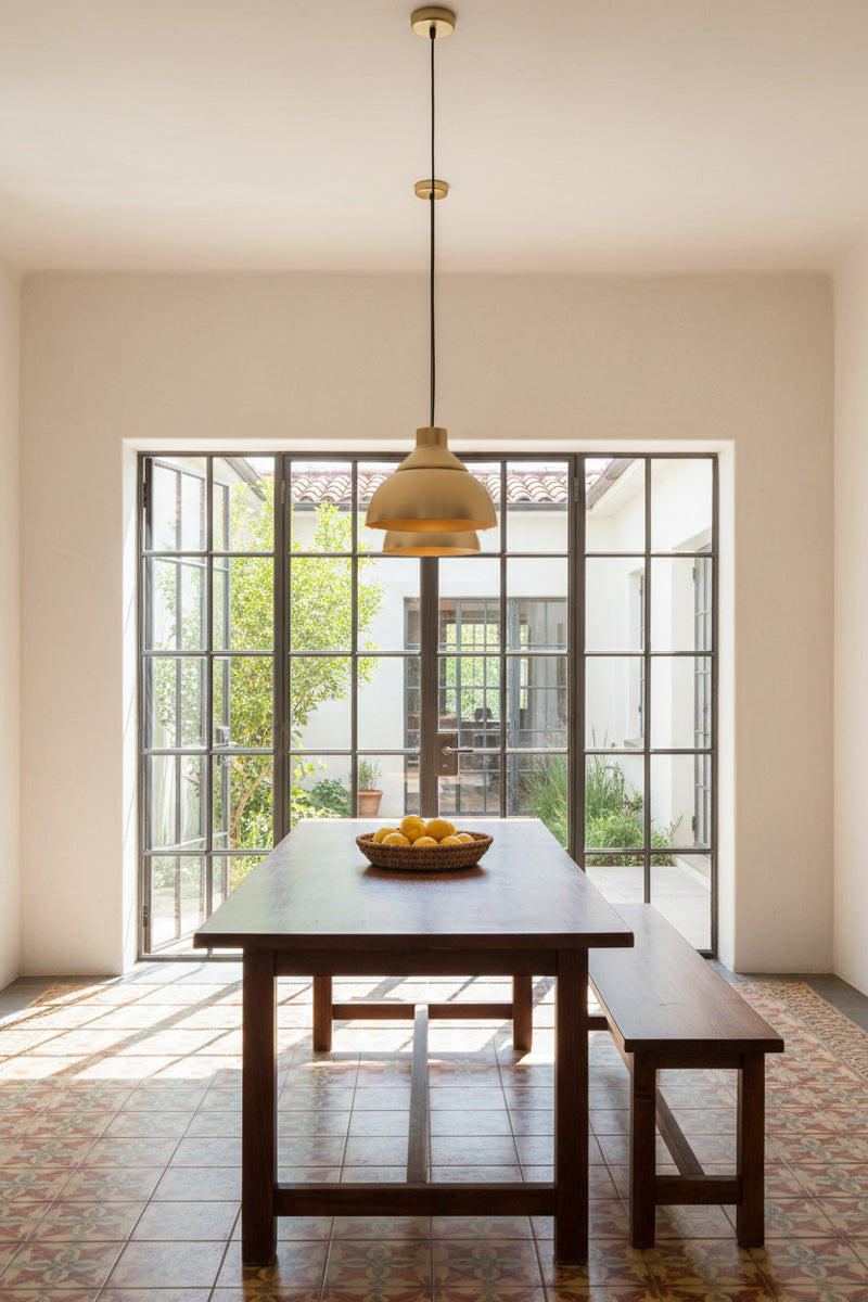 A modern dining room, dark wood rectangular table with matching benches, and two gold brass dome-shaped pendant light hanging above