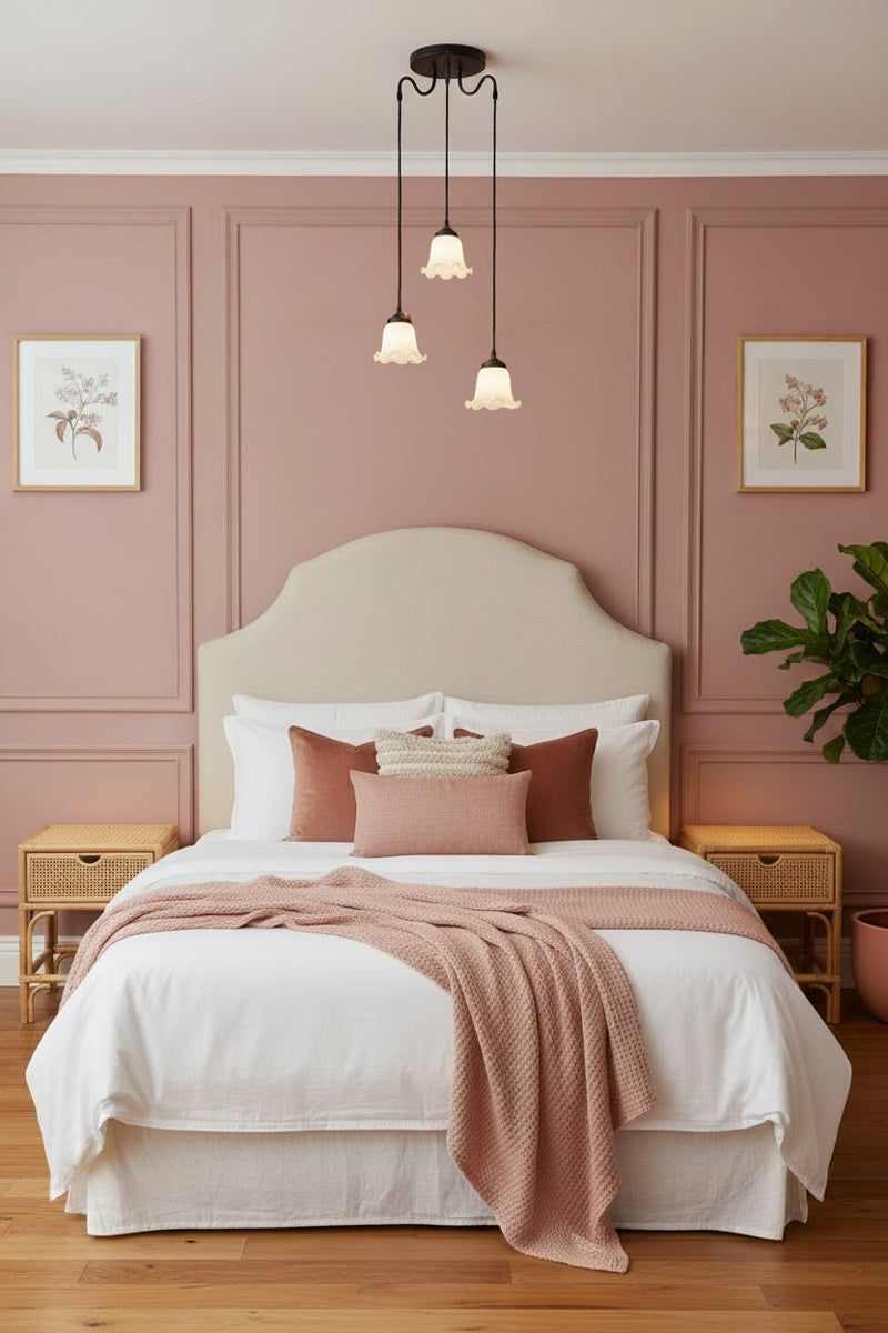 Three light pendant with gooseneck arm, black cords and opal glass shades hanging in a muted pink bedroom with plush furniture and elegant decor. 