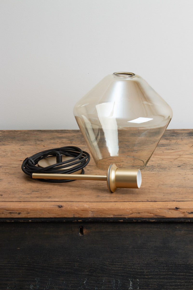 Lugano Glass Pendant Light shade B in champagne glass with gold brass fitting and black braided cord, placed uninstalled on a timber bench 