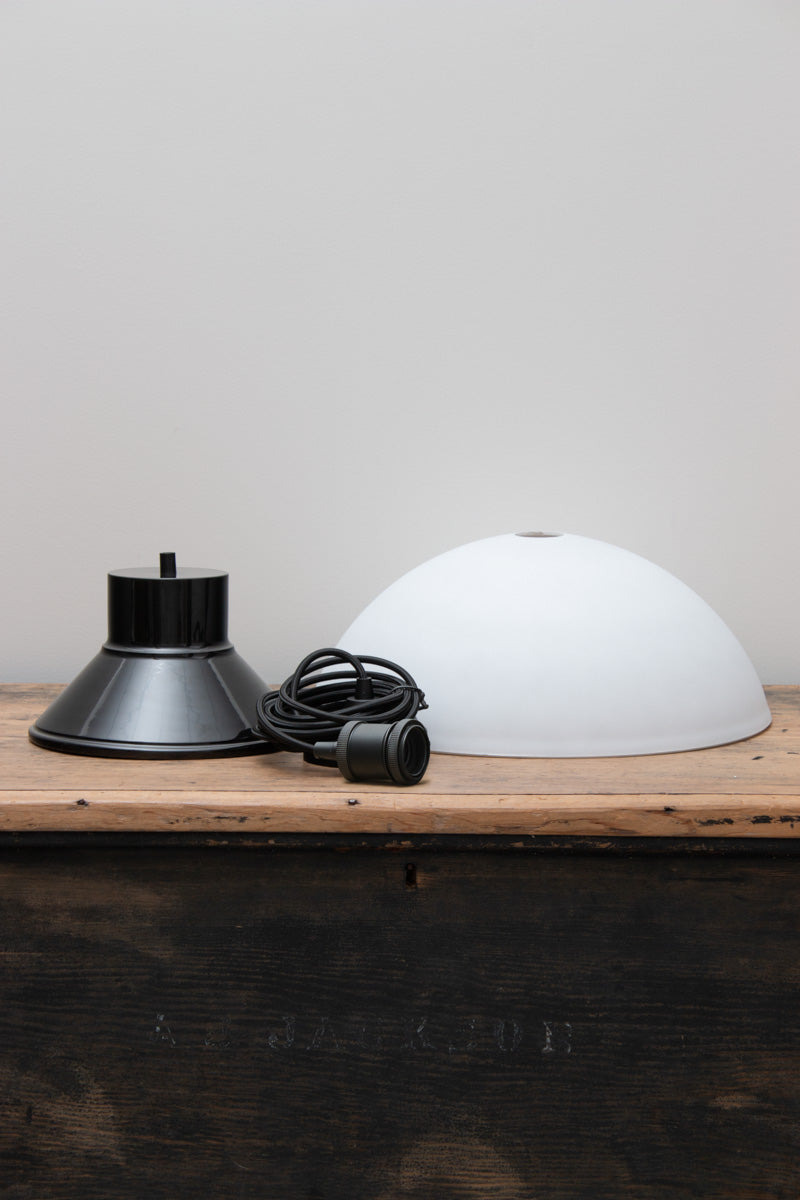 Uninstalled Homestead Foundry Pendant Light with a black shade cover and opal glass done shade, placed on a timber bench. 