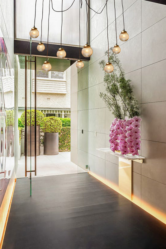 9 drop sweeping chandelier with amber reeded glass ball shades and gold/brass galleries, installed in a modern home entrance. 