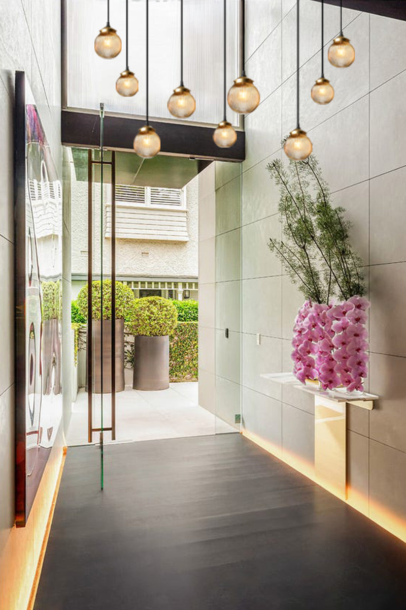 9 drop sweeping chandelier with amber reeded glass ball shades and gold/brass galleries, installed in a modern home entrance. 