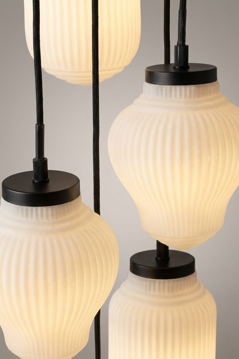close up of 5 drop pendant light with 5 mixed ribbed, translucent warm-white glass shades and black metal fittings.