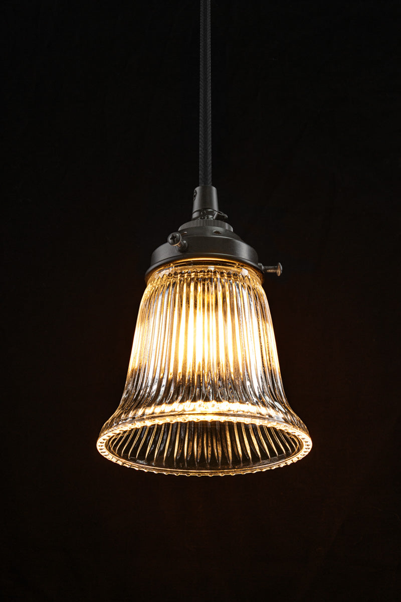 Small ribbed clear glass pendant light with black hardware and cord in dark room. 