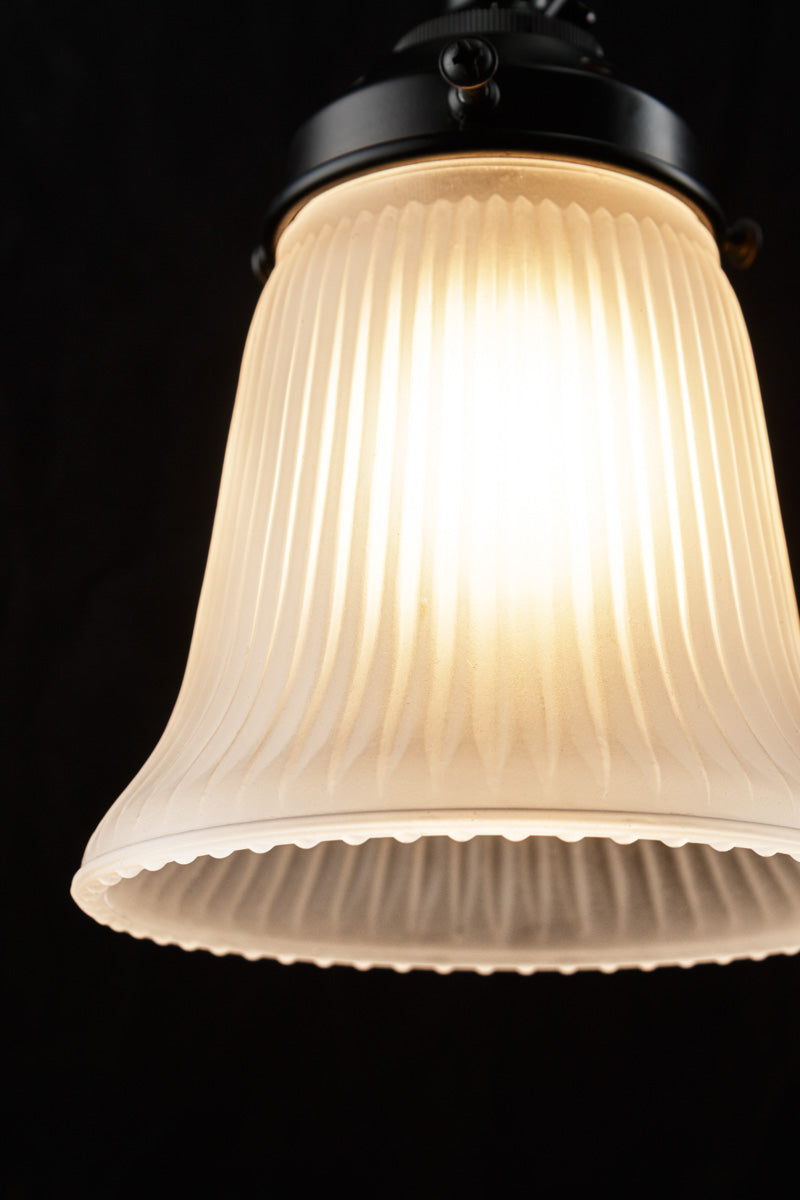 Close up of the small holophane opal glass shade on black hardeware with light on in a dark room- showcasing shade deatiling.