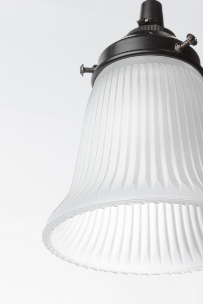 Close up of the ribbed opal glass pendant light with black hardware and cord. 