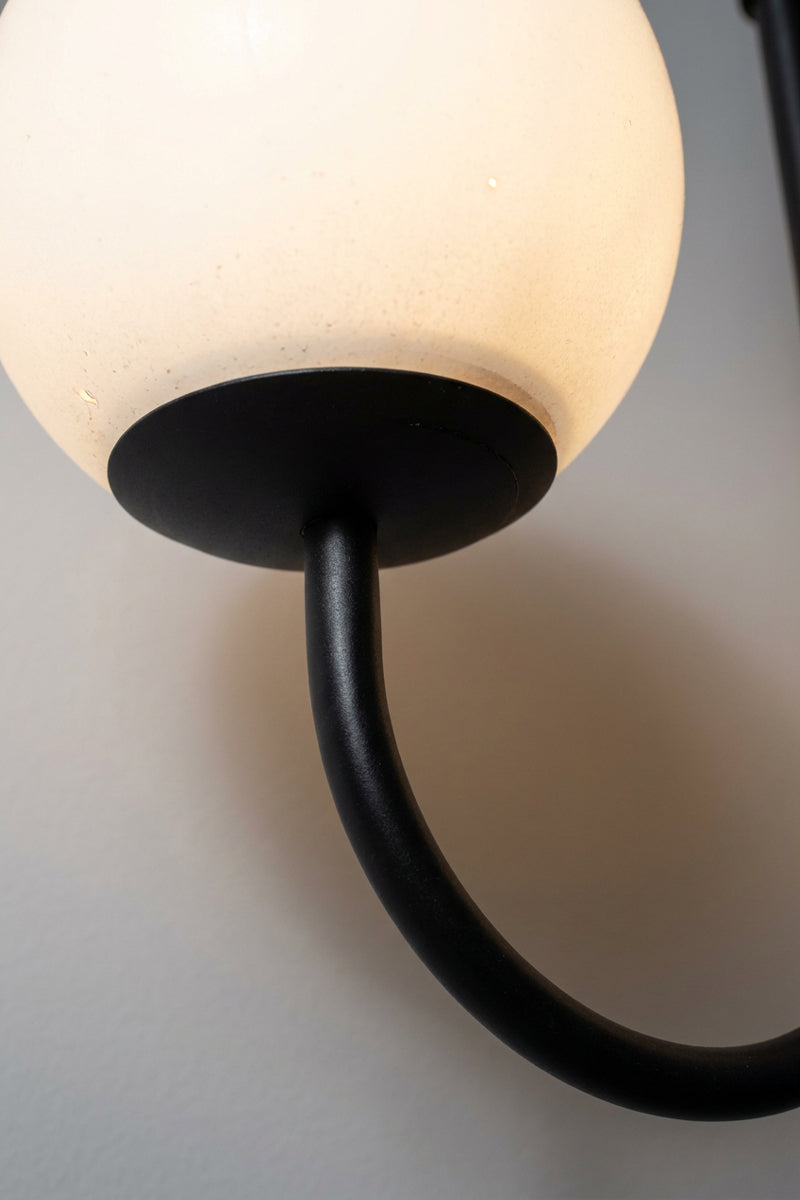 Close-up of an illuminated opal glass globe and curved black metal arm on the Bonnie Double Chandelier
