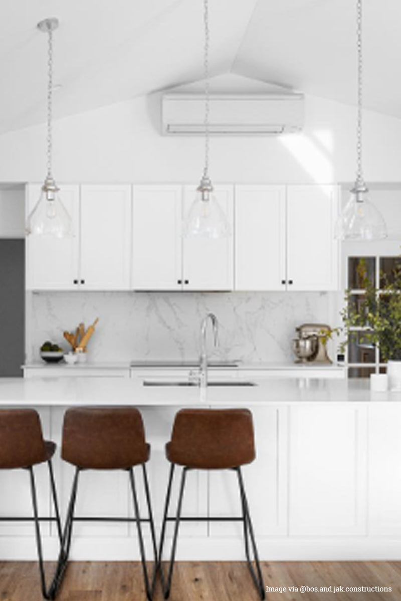 Image via @ bos.and.jak.constructions: 3 glass pendant lights with chrome fixtures in a bright white kitchen. 
