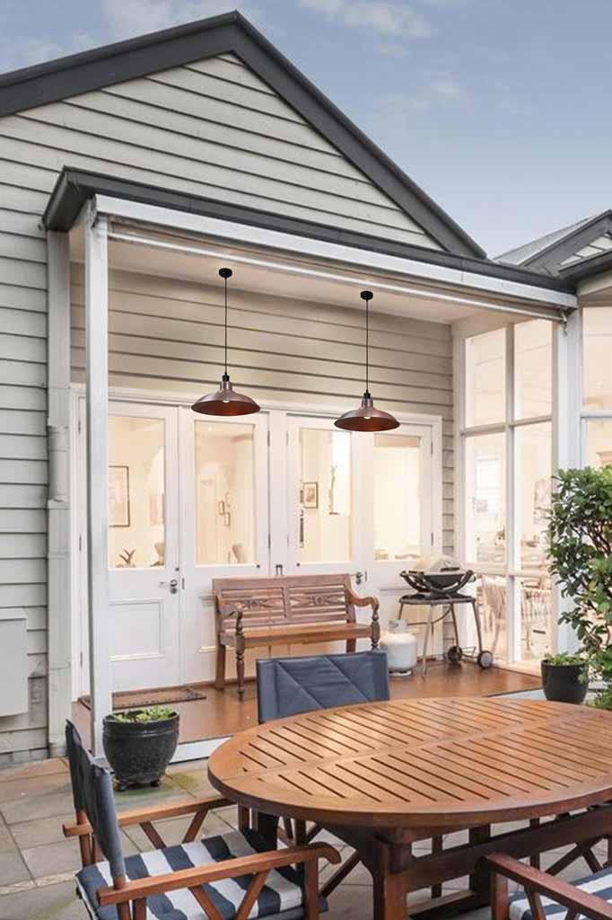 Two outdoor pendant lights on black cable with two solid copper shades, hanging under a small patio. 
