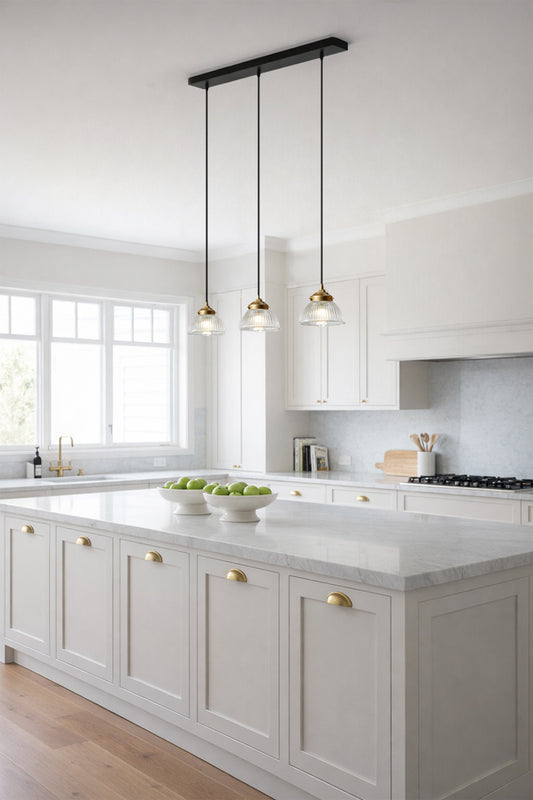 Modern kitchen with white cabinets, marble countertops and Come glass shade pendant on a linear pendant