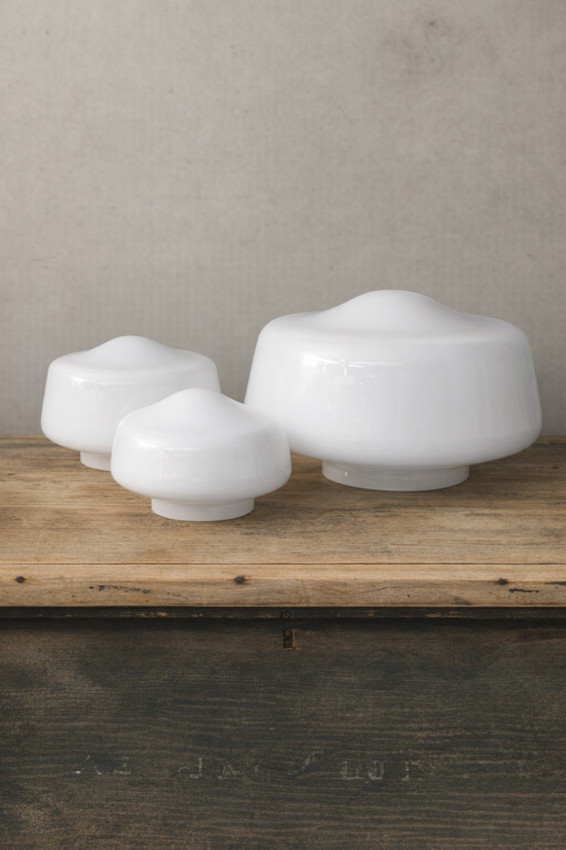 Three opal glass light shades placed uninstalled on a timber bench showcasing their small, medium and large sizes. 