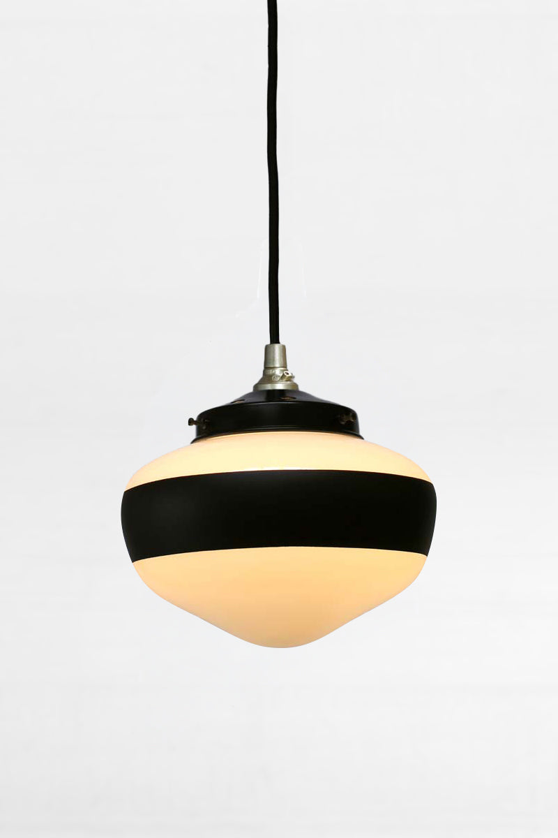 Small opal glass shade with hand painted black stripe paired with a fabric cord with gold hardware and a black gallery. 