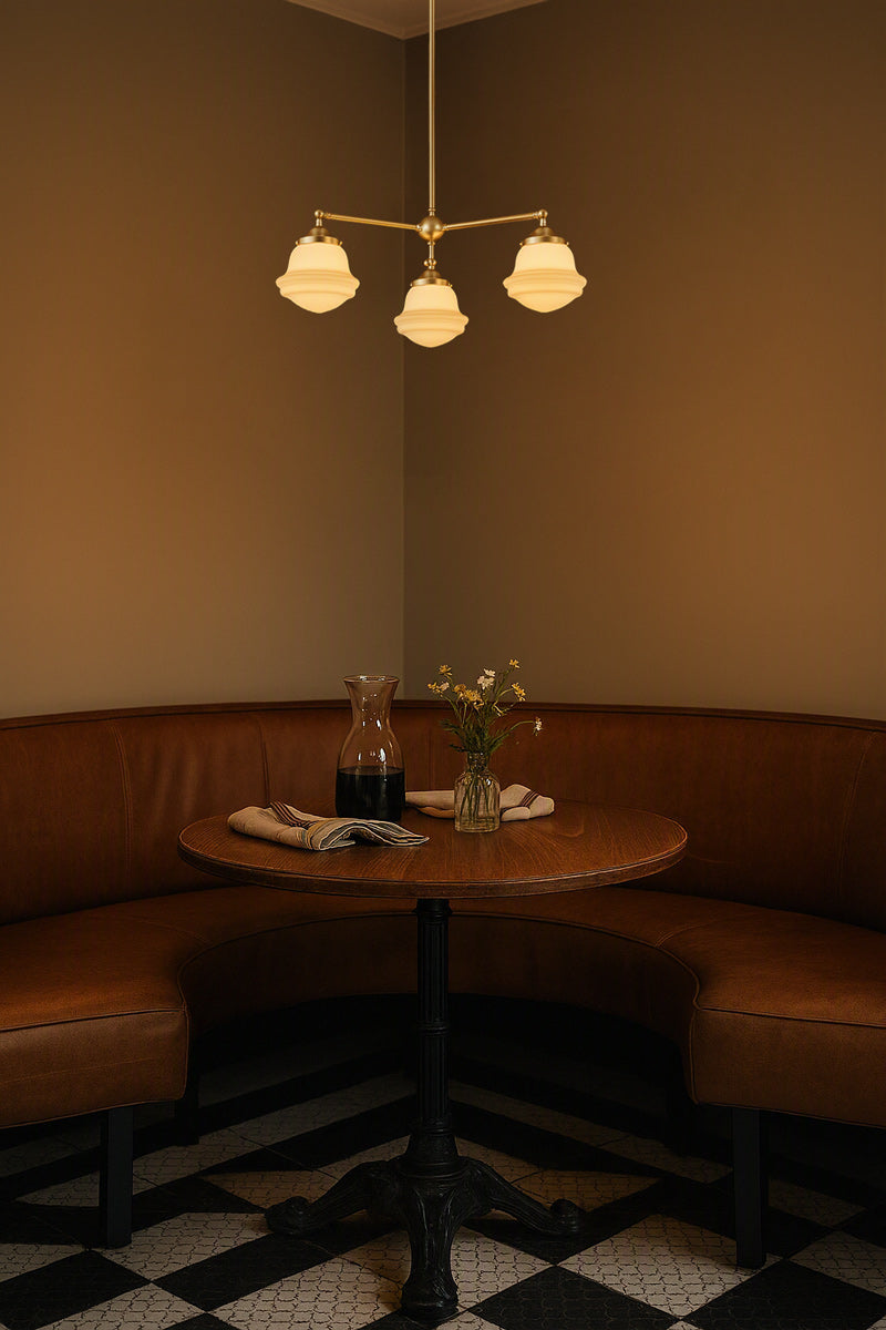 Gold/brass three arm chandelier with opal glass shades over a brown leather corner booth. 
