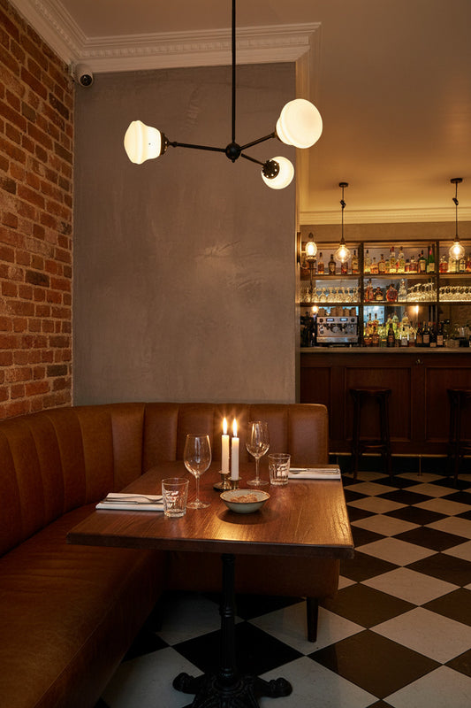 Black three arm chandelier with opal glass shades over a brown leather bench in a restaurant.