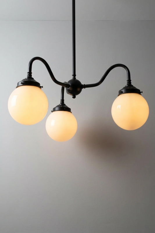 Black three light pendant with opal glass globes on curved arms, lit against a plain grey backdrop