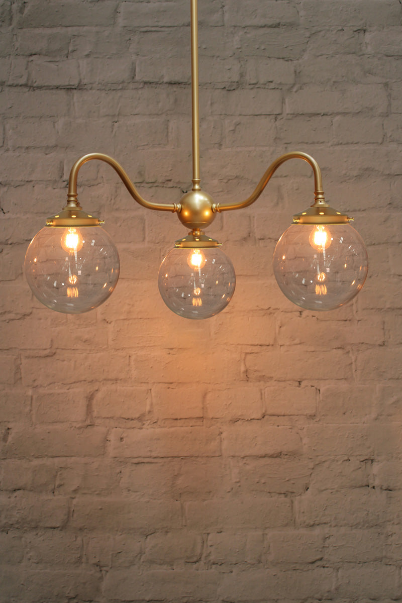 Small, opal clear ball shades on a triple gold/brass gooseneck chandelier fixture. 