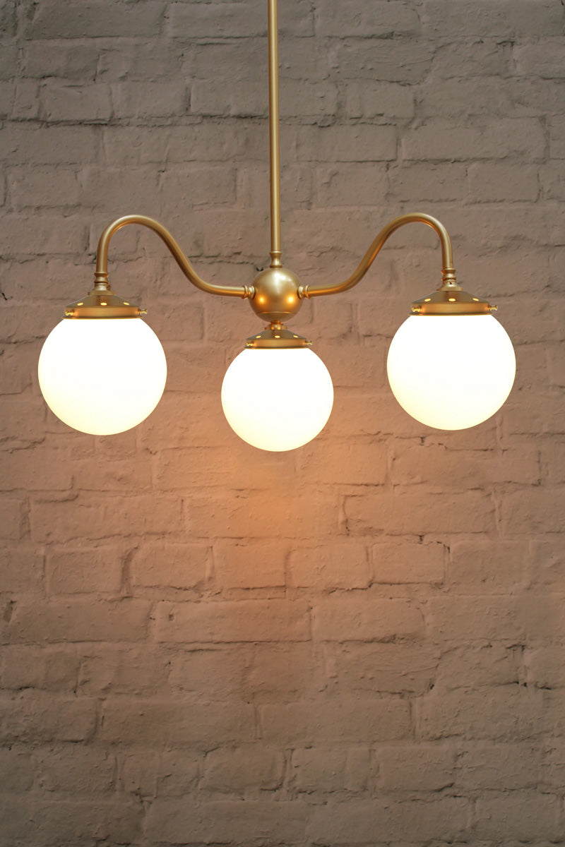 Small, opal glass ball shades on a triple gold/brass gooseneck chandelier fixture. 